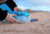 hand cleaning up single-use plastic bottle off of beach