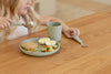 Child eating lunch from a silicone plate with silicone utensils and silicone cup.