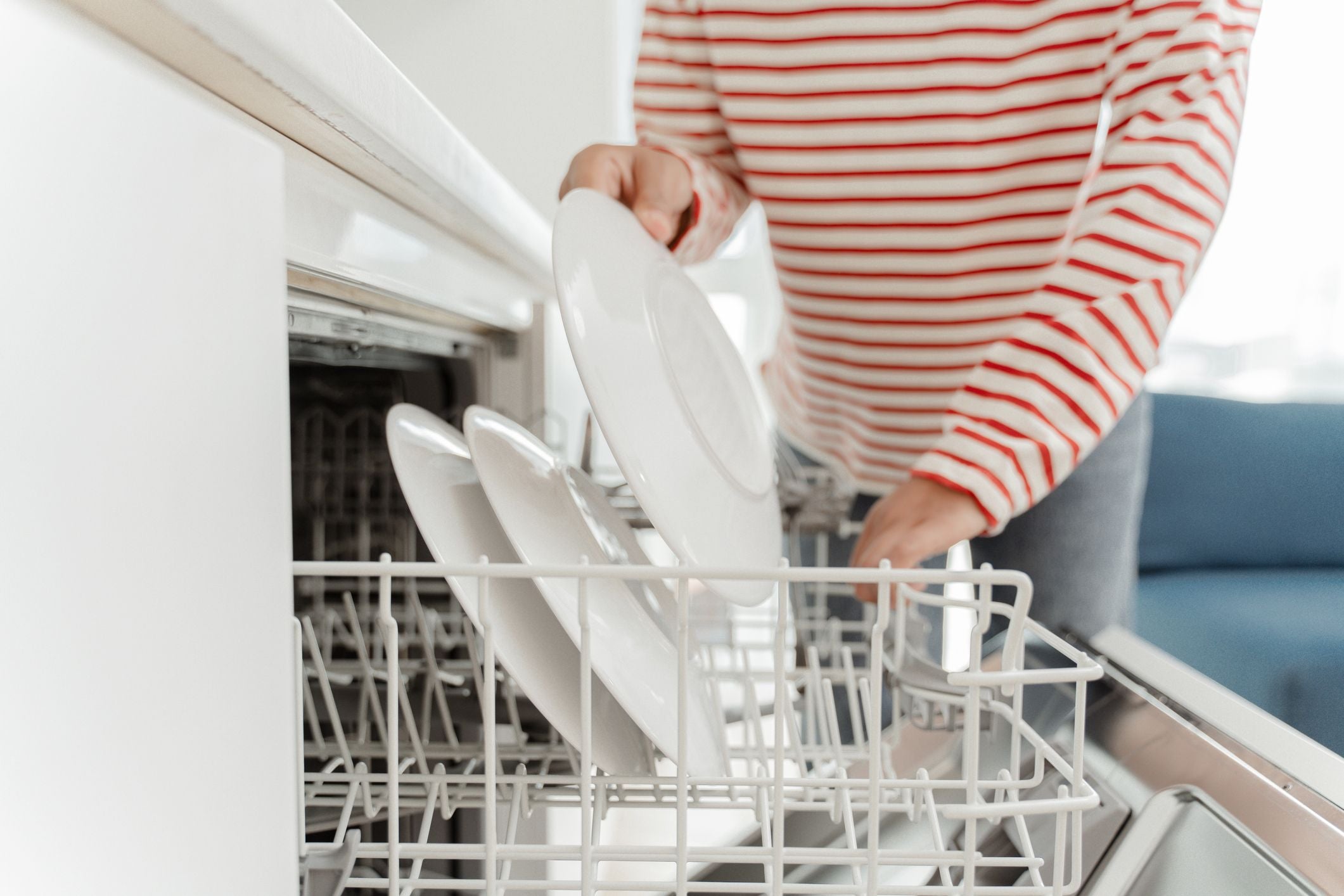 Person loading a dishwasher with white plates