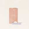 A cylindrical, peach-colored container labeled BLUELAND Oxi Laundry Booster stands upright, with its lid off and resting in front, revealing white powder inside. The background is plain and light-colored.